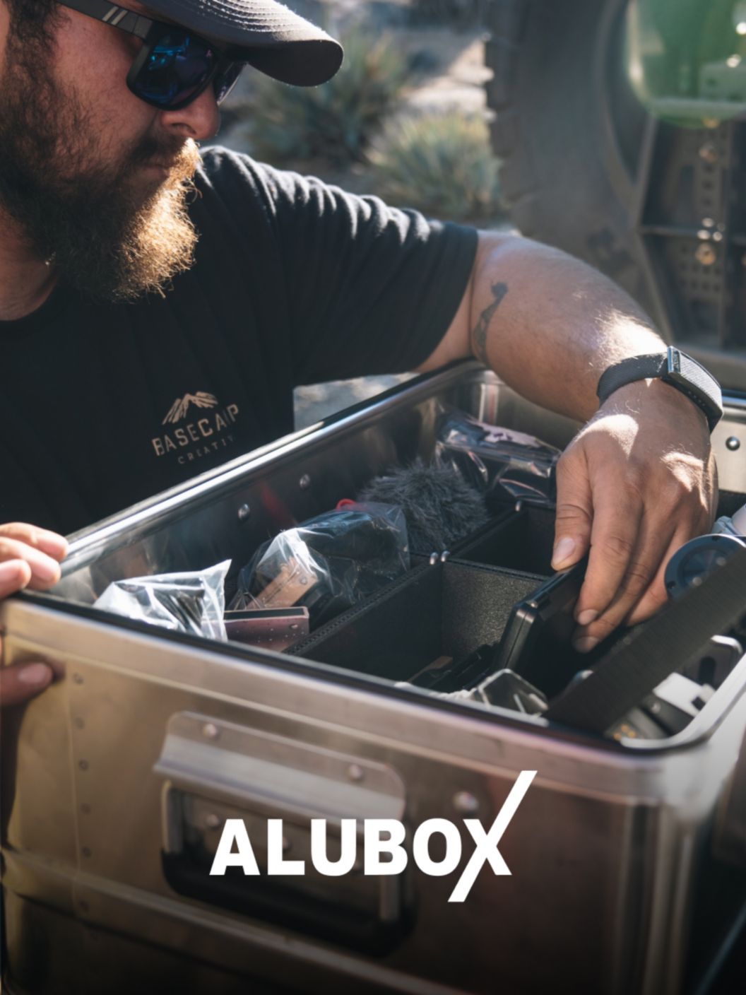 A bearded man looks through an open Alubox full of camping gear. 